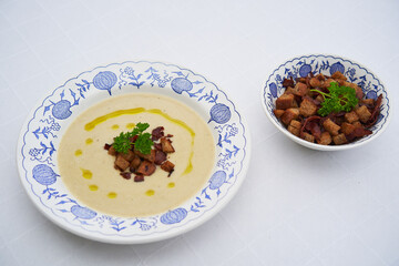 Delicious tender vegetarian celery soup served with roasted bread crumbs and sprinkled by extra virgin olive oil in vintage deep porcelain plate with extra bread crumbs in small bowl as a side dish.