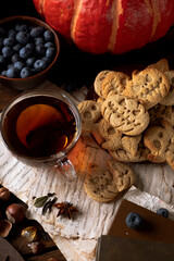 Cookies in the shape of pumpkins and ghosts are in a plate on the table. Next to a teapot and mugs, an autumn still life