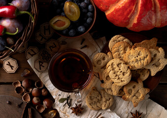 Cookies in the shape of pumpkins and ghosts are in a plate on the table. Next to a teapot and mugs, an autumn still life