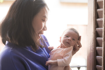 Fototapeta premium lifestyle shot on young and happy Asian Chinese woman holding tenderly her adorable newborn baby girl in her arms in mother and daughter love and care concept