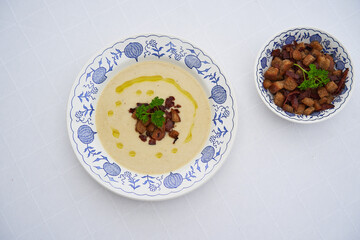 Top view picture of deep rustic plate with delicious traditional creamy celery root soup served with bread crumbs in the small bowl, parsley and extra virgin olive oil. Healty dish full of nutritions.