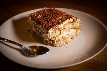 Slice of Italian Tiramisu made of coffee, chocolate, mascarpone, sponge cake and cream on a plate with a spoon
