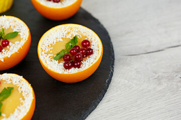 Sweet dessert with red currant and coconut flakes in orange on black plate