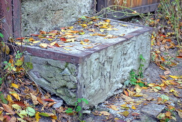 a large step of a gray concrete threshold with a brown iron corner on the ground in fallen dry...