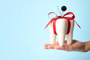 Hand with white tooth model with bow ribbon on a blue background