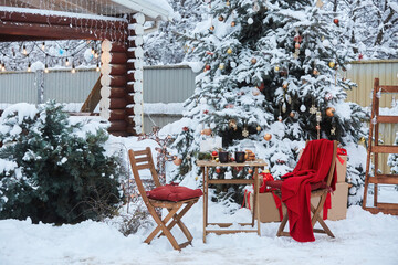 New Year and Christmas decoration of the yard. Snow-covered exterior with a table and chairs. The red color of the plaid.