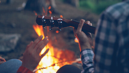 Close-up shot of male hands playing the guitar and female hands moving in dance with burning...