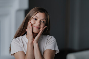 Adorable brunette young woman touching face looking aside cute smiling. Pretty hispanic girl in white t-shirt satisfied by health and her skin care products. Beauty and healthy lifestyle. Women health