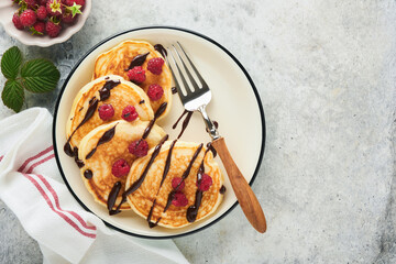 American pancakes. Pancakes with fresh raspberry with chocolate glaze or toppings in gray bowl on light gray table background. Homemade classic american pancakes. Page for magazine concept. Top view.