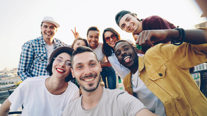Point of view shot of bearded young man looking at camera taking selfie with friends sitting on...
