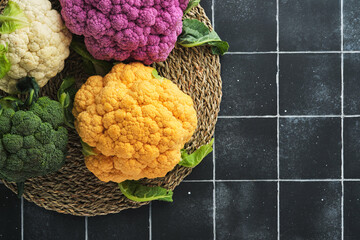 Colorful cauliflower. Various sort of cauliflower on old stone tiles black concrete background. Purple, yellow, white and green color cabbages. Broccoli and Romanesco. Agricultural harvest. Mock up.