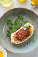 Rustic plate with whole grilled haloumi cheese, fresh parsley and basil, vertical shot, high angle view, middle close-up