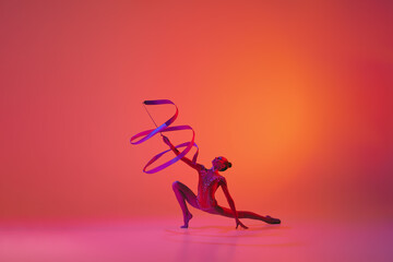 Young flexible teen girl rhythmic gymnast in motion, action isolated over pink background in neon...
