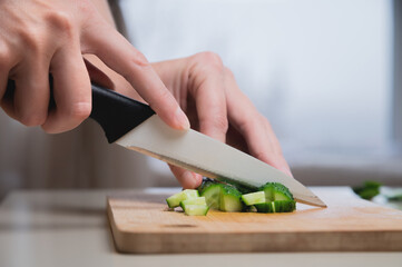 close-up of female hands cutting on wooden cutting board fresh green cucumber for salad, home food and cooking