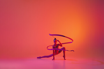 Studio shot of young charming girl, rhythmic gymnast training with sports equipment isolated over pink background in neon light filter