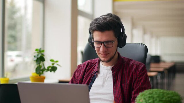 Developer, video editor man in headphones working with laptop at spacious coworking alone enjoying music. Stylish creative musician producer listens song in office alone. Online gamer playing games.