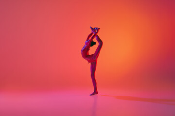 Fototapeta na wymiar Young flexible teen girl rhythmic gymnast in motion, action isolated over pink background in neon light. Sport, beauty, competition, flexibility, active lifestyle