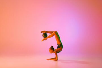Fototapeta na wymiar Studio shot of young charming girl, rhythmic gymnast training with sports equipment isolated over pink background in neon light filter