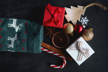 Christmas stocking filled with small presents, sweets and various decorations. Dark background, flat lay.