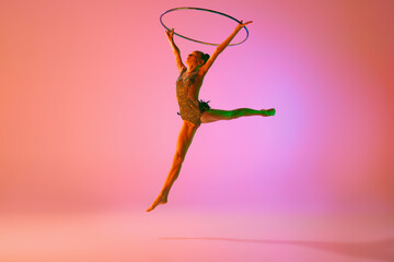 Studio shot of young charming girl, rhythmic gymnast training with sports equipment isolated over...