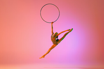Beautiful and flexible graceful athlete rhythmic gymnastic artist dancing, doing stretch exercises isolated on colorful background in neon. Beauty, art, sport