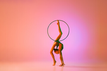 Beautiful and flexible graceful athlete rhythmic gymnastic artist dancing, doing stretch exercises isolated on colorful background in neon. Beauty, art, sport