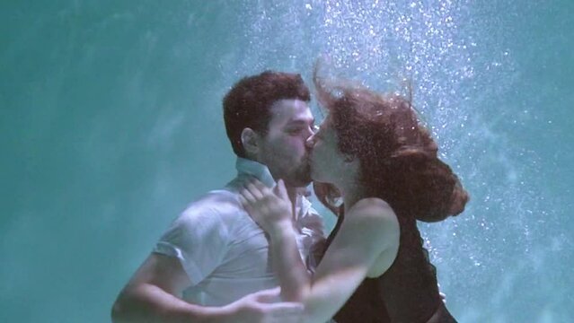 A woman and a guy are swimming underwater. A woman kisses a guy underwater.