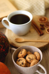 Cup of tea or coffee, seasonal spices, bowl of cookies, blanket, pumpkins, colorful leaves, books and tangerines on wooden table. Cozy hygge at home. Selective focus.