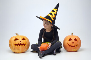 Fototapeta premium portrait of a charming little girl in a witch costume, Jack's lamps are standing around. the concept of the heluin holiday