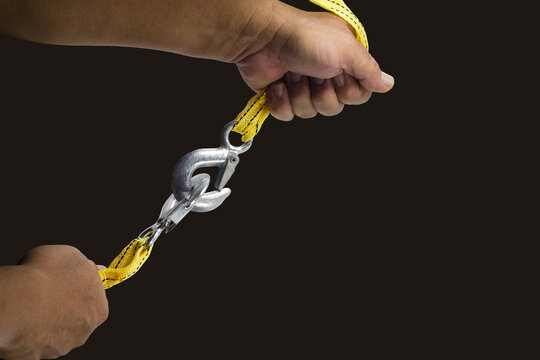 Isolated image of yellow nylon webbing with white steel hooks pulled with both hands on a black background, suitable for use as backgrounds and textures.