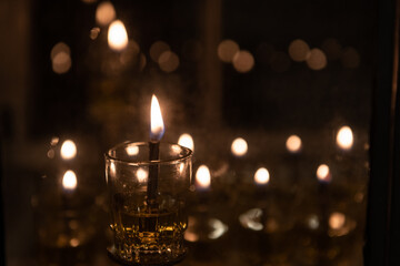 The shamash, or additional helper candle on the menorah, glows brightly in this artistic image of oil Hanukkah candles burning in a glass housing during the Festival of Lights in Israel.