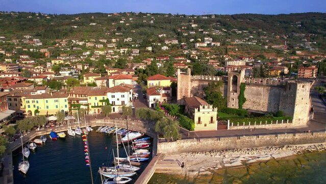 Italy Lake Garda aerial drone fly-out from Torri del Benaco castle and round marina at sunset. Scenic medieval village and harbor reveal near Verona. Luxury travel destination Lago di Garda 4k 