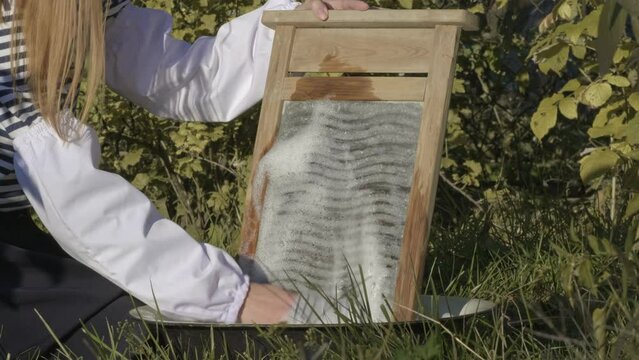 Close-up of a woman's hands washing clothes on old vintage washboard outdoors in summer day. Antique Washboard. Woman washing on a retro washboard. Washerwoman doing laundry by hand