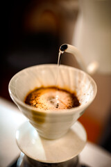 Barista making a Geisha coffee, pouring hot water from kettle over a ground coffee powder