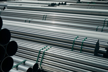 There are stacks of new stainless steel pipes on the open storage area, pipes of different...