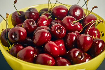 On the table there is a yellow glass cup filled to the top with ripe cherries, dark red berries, juicy and delicious, a simple homemade still life