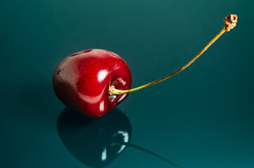 Cherry berry lies on a colored glass surface, dark red berry, ripe and juicy, minimalist still life