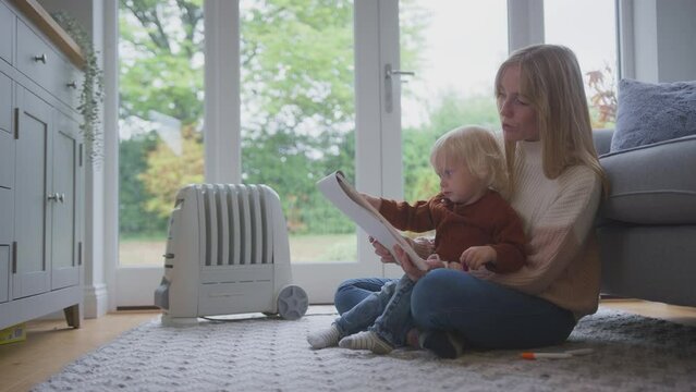 Mother and son sitting on floor next to portable plug in radiator drawing picture and trying to keep warm during energy crisis - shot in slow motion