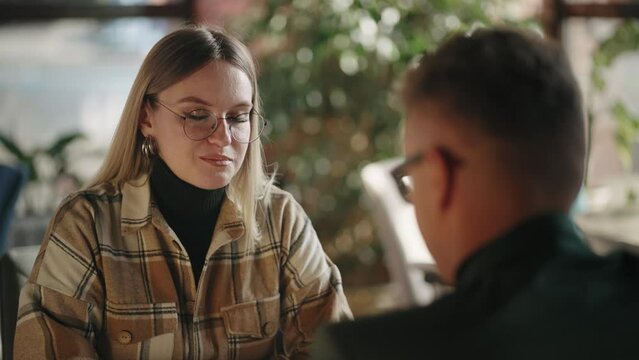 Man with glasses conducts negotiations talks and conducts a job interview or discusses issues with a woman sitting at a table. Business meeting of a man and a woman, a dialogue between two partners