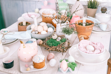 Obraz na płótnie Canvas happy easter and spring holidays time. festive tablescape set decor. traditional dinner food easter eggs and baked cakes on table at home. rabbit and willow. pale pop pastel blue and pink color