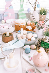 Fototapeta na wymiar happy easter and spring holidays time. festive tablescape set decor. traditional dinner food easter eggs and baked cakes on table at home. rabbit and willow. pale pop pastel blue and pink color