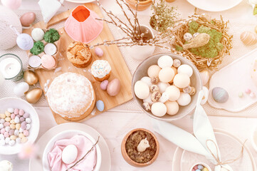 Fototapeta na wymiar happy easter and spring holidays time. festive tablescape set decor. traditional dinner food easter eggs and baked cakes on table at home. pale pop pastel blue and pink color. top view. flare