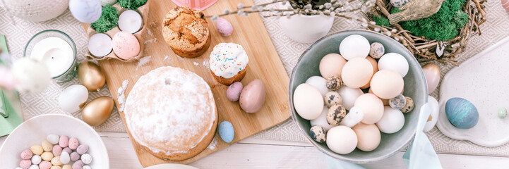 happy easter and spring holidays time. festive tablescape set decor. traditional dinner food easter eggs and baked cakes on table at home. pale pop pastel blue and pink color. top view. banner