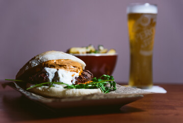 Inviting meat cheeseburger with white and red sauce and lettuce on table with beer and potato fries in the background. Delicious dinner with meat and hamburger at a restaurant