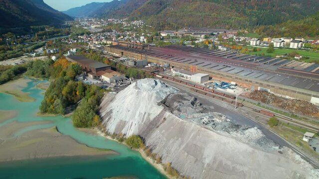AERIAL: Industrial infrastructure near city and mountains in vibrant fall season. Steel factory located by the river in picturesque valley surrounded with alpine landscape in colorful autumn shades.