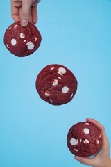 Gordijnen Hands holding chocolate cookies on a blue background, vertical © Nina Ljusic/Wirestock Creators