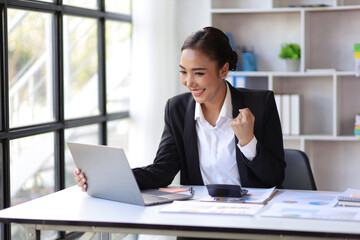 Businesswoman in office looking at laptop screen and showing excitement and joy about a successful business project.