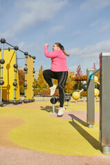 Outdoor training. Weight lost concept. Young woman doing fitness exercises at street public sports ground. Sunny autumn day. Sport, health, plans, body positive