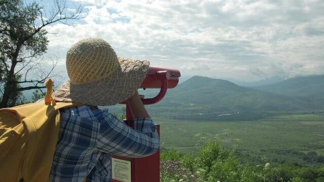 Woman looking through coin operated binoculars on mountains. Female feels freedom on sunny day. Cheerful woman enjoy outdoor lifestyle on summer vacation trip