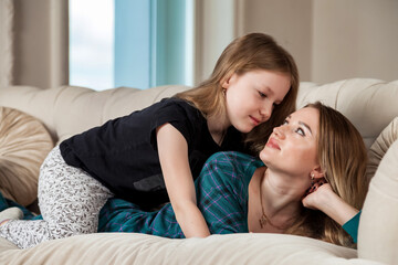 Happy cute mom and teen girl daughter in casual clothes playfully together on sofa in living room at home. Concept of spending time together with kids and family lovely relationships. Copy text space